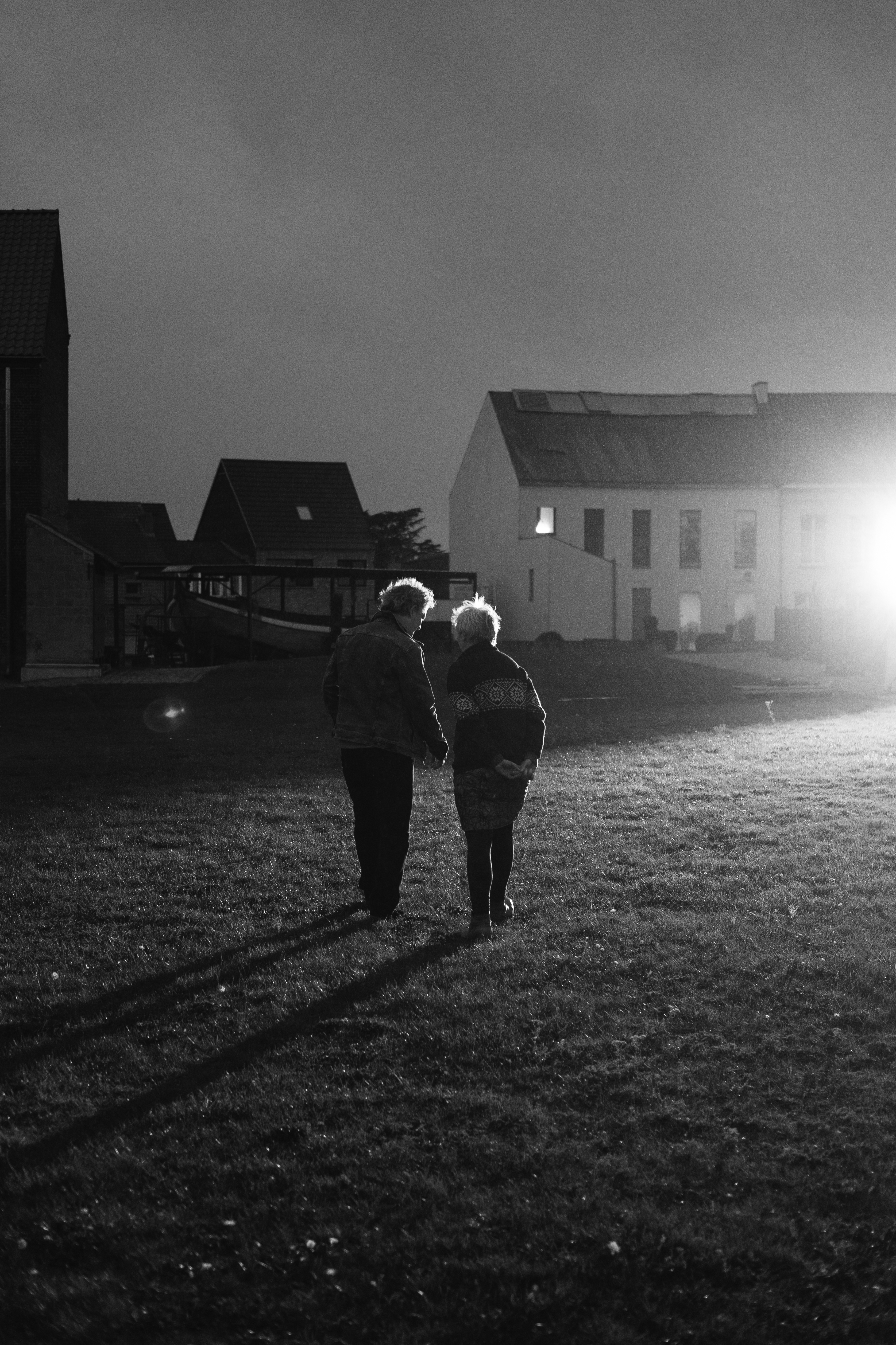 Twee mensen (broer en zus) lopen in gesprek naast elkaar, weg van de camera en naar een licht toe. De foto is genomen op de set van Ik Zie Jou.